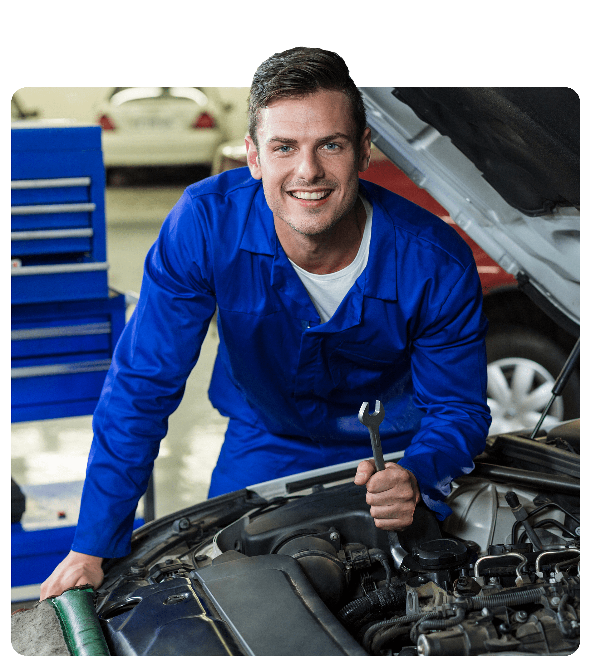 Mechanic in blue overalls, leaning against a cars engine, holding a spanner and smiling